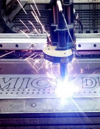 CNC plasma torch cutting lettering into a stainless steel plate, throwing sparks across the cutting table
