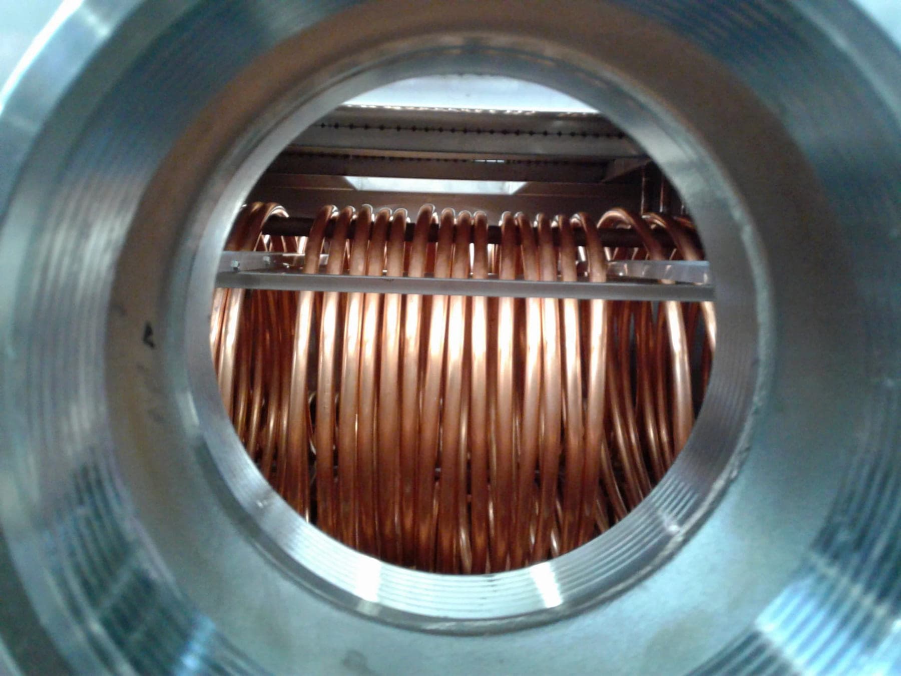 Copper heat exchange coils seen through a six-inch port in a stainless steel tank