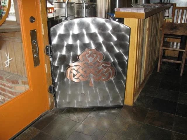 Custom stainless steel door with a decorative Celtic knotwork cutout installed in a restaurant entryway