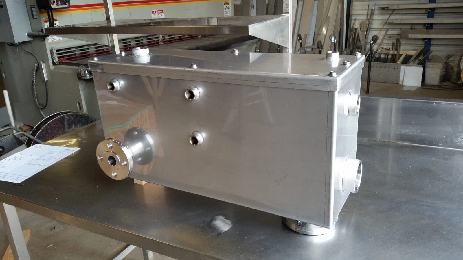 Rectangular stainless steel vessel with multiple threaded couplings and a flanged connection on a shop table