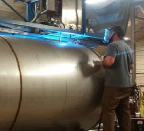 Swhift fabricator finishing the shell of a large horizontal stainless steel tank in the shop