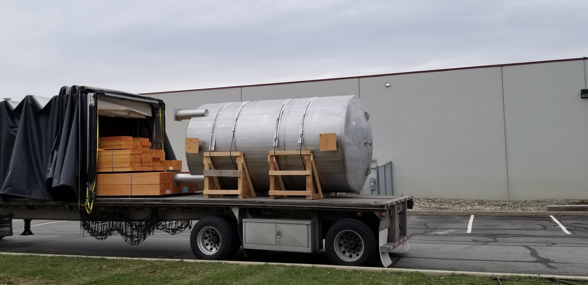 Horizontal stainless steel pressure tank cradled on timber and strapped to a flatbed trailer