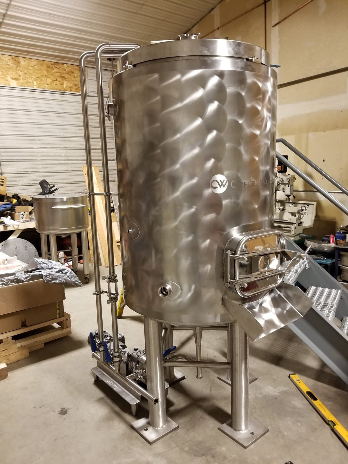 Jacketed stainless steel vertical tank with a side manway, sanitary fittings and a pump skid
