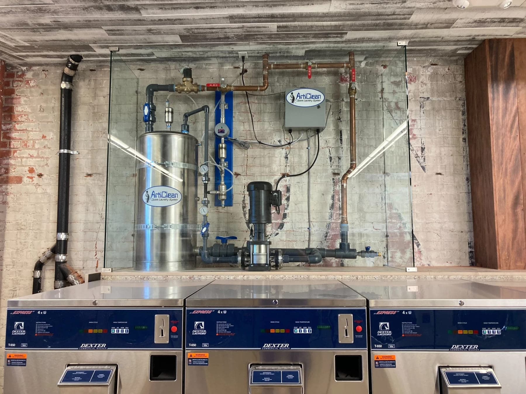 Stainless steel ozone contact tank and circulation pump installed behind glass above commercial washers