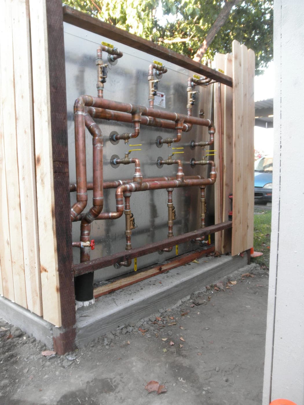 Rectangular stainless steel storage tank installed outdoors with a copper supply and return manifold