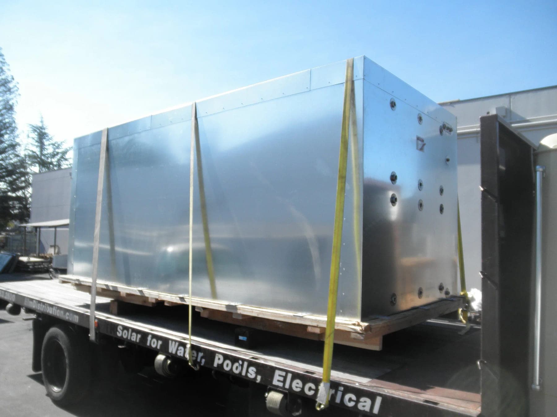 Large rectangular stainless steel tank strapped to a flatbed truck for delivery