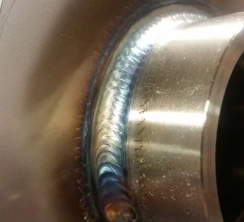 Close-up of a continuous TIG weld bead where a fitting joins a stainless steel tank wall